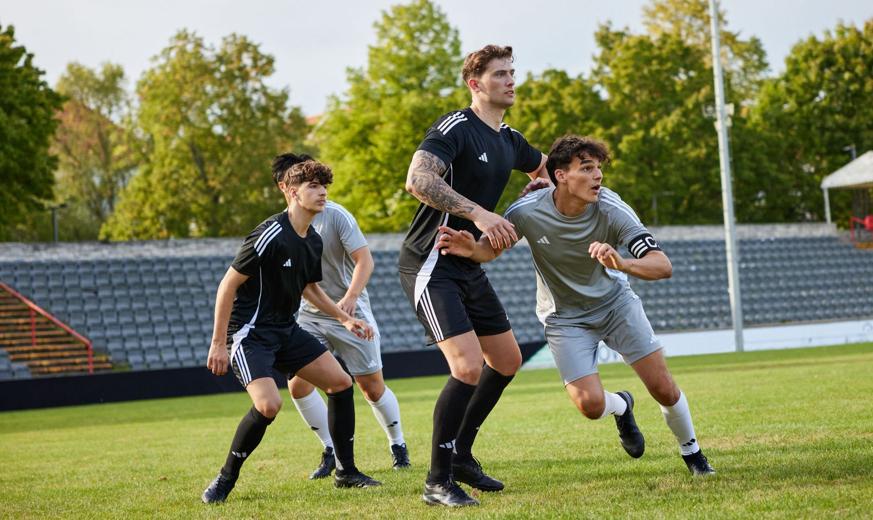 Four soccer players wearing Customised Adidas kits in action on a grass field with trees in the background